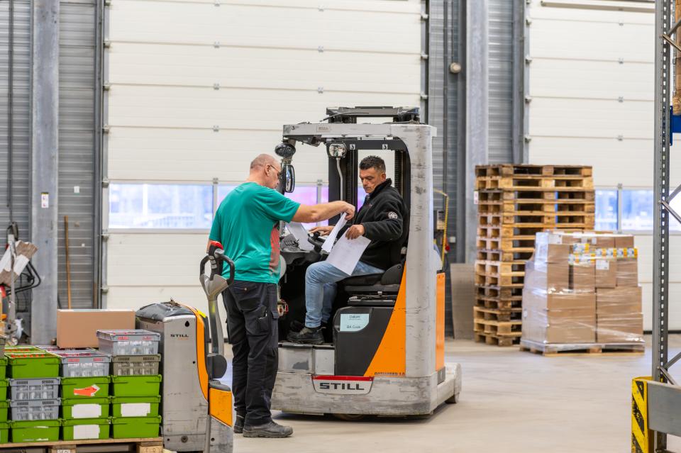 Een medewerker geeft een pakbon aan een heftruckchauffeur