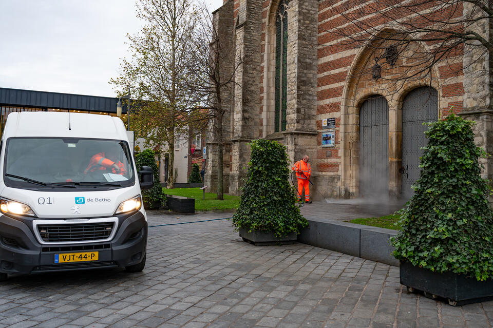 Een schoonmaakmedewerker spuit de straat voor de kerk schoon